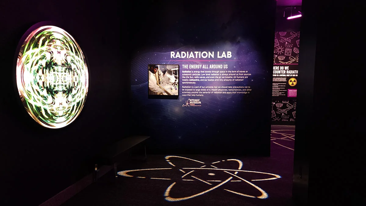 Radiation Lab museum exhibit with glowing wall panels and an atomic symbol projected on the floor.