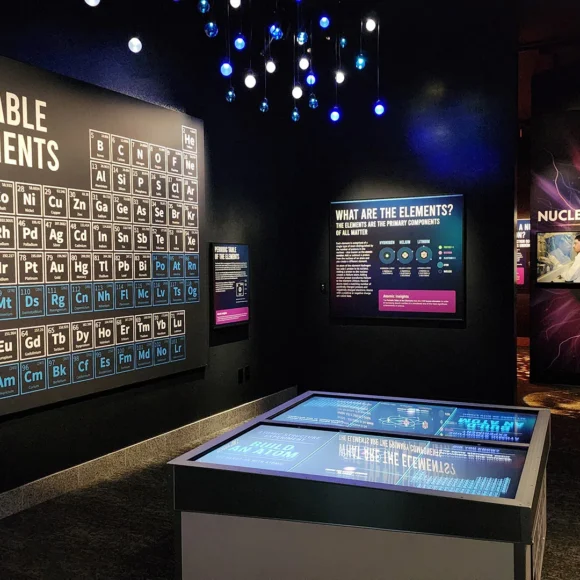 Periodic Table wall display, interactive touchscreen table, and Nuclear Reactions Lab exhibit in a museum.