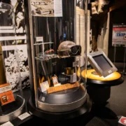 Display cases with an artillery shell, military helmet, and an interactive kiosk in a museum.