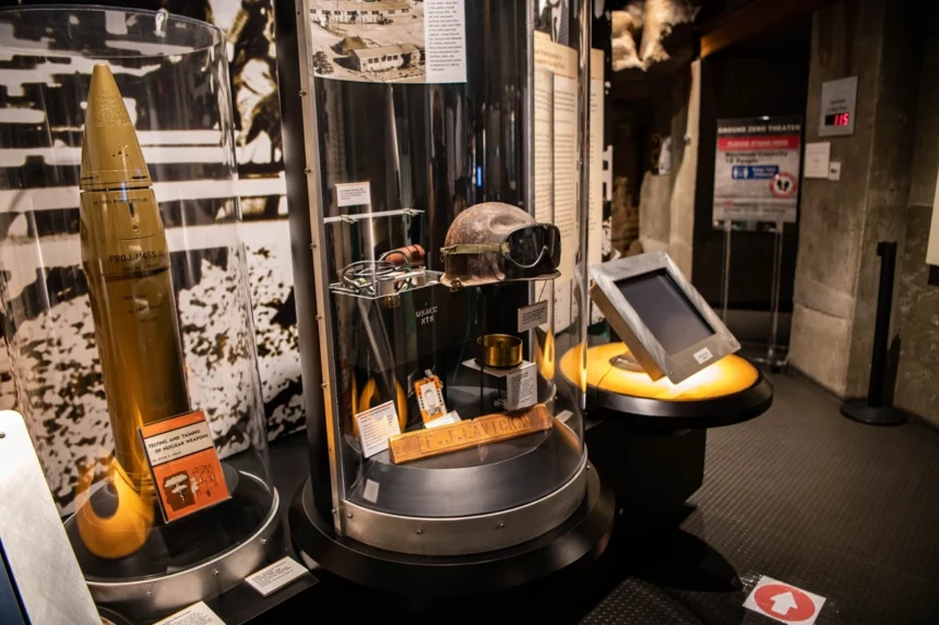 Display cases with an artillery shell, military helmet, and an interactive kiosk in a museum.