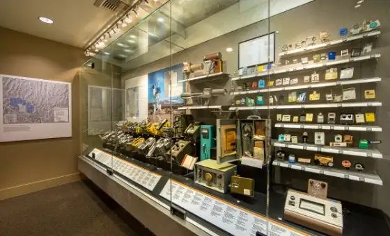 Museum glass case filled with historical radiation monitoring equipment and badges.