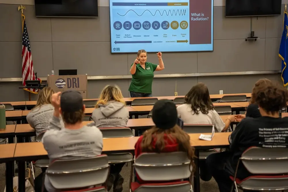 Presenter speaking to a group of students seated in a lecture hall during a presentation