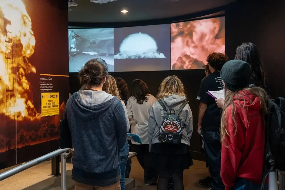 Group of students gathered around a guide looking at a historic military artifact exhibit